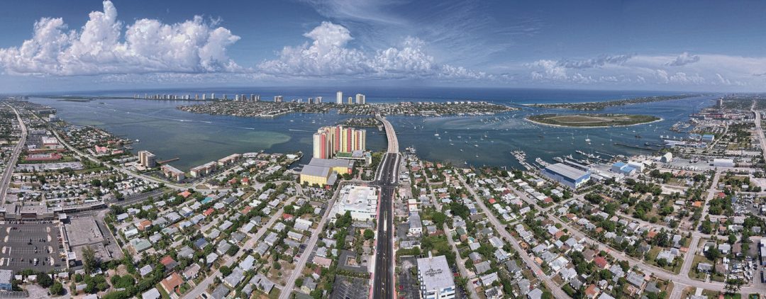 Aerial panorama of Riviera Beach: Blue Heron Boulevard running toward the Blue Heron Bridge, with the Intracoastal Waterway and Singer Island beyond.