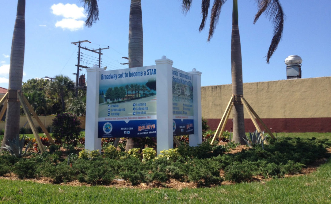 A CRA development sign for the Broadway corridor improvement plan, surrounded by new palms and landscaping.