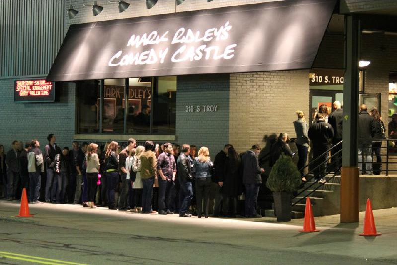 Guests lined up at night outside Mark Ridley's Comedy Castle beneath its lit sign