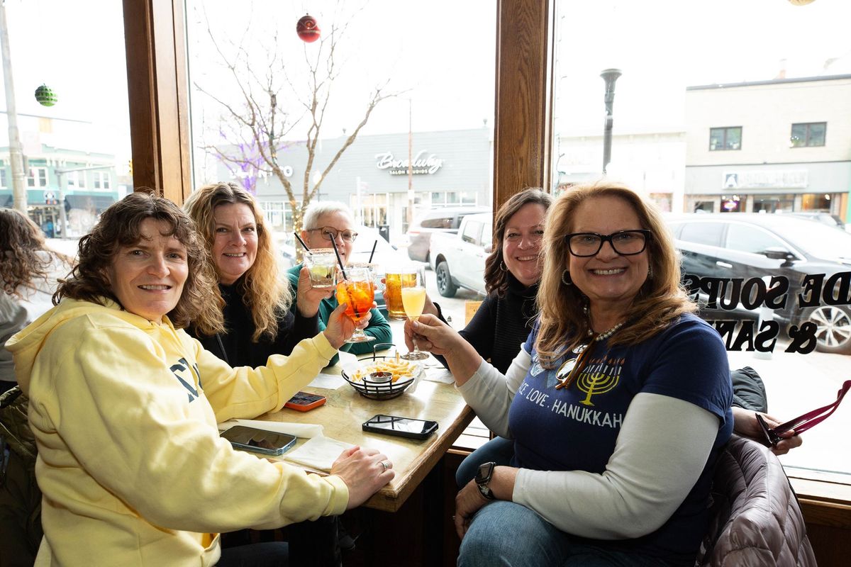 Friends raising cocktails at a window table in a downtown Royal Oak restaurant