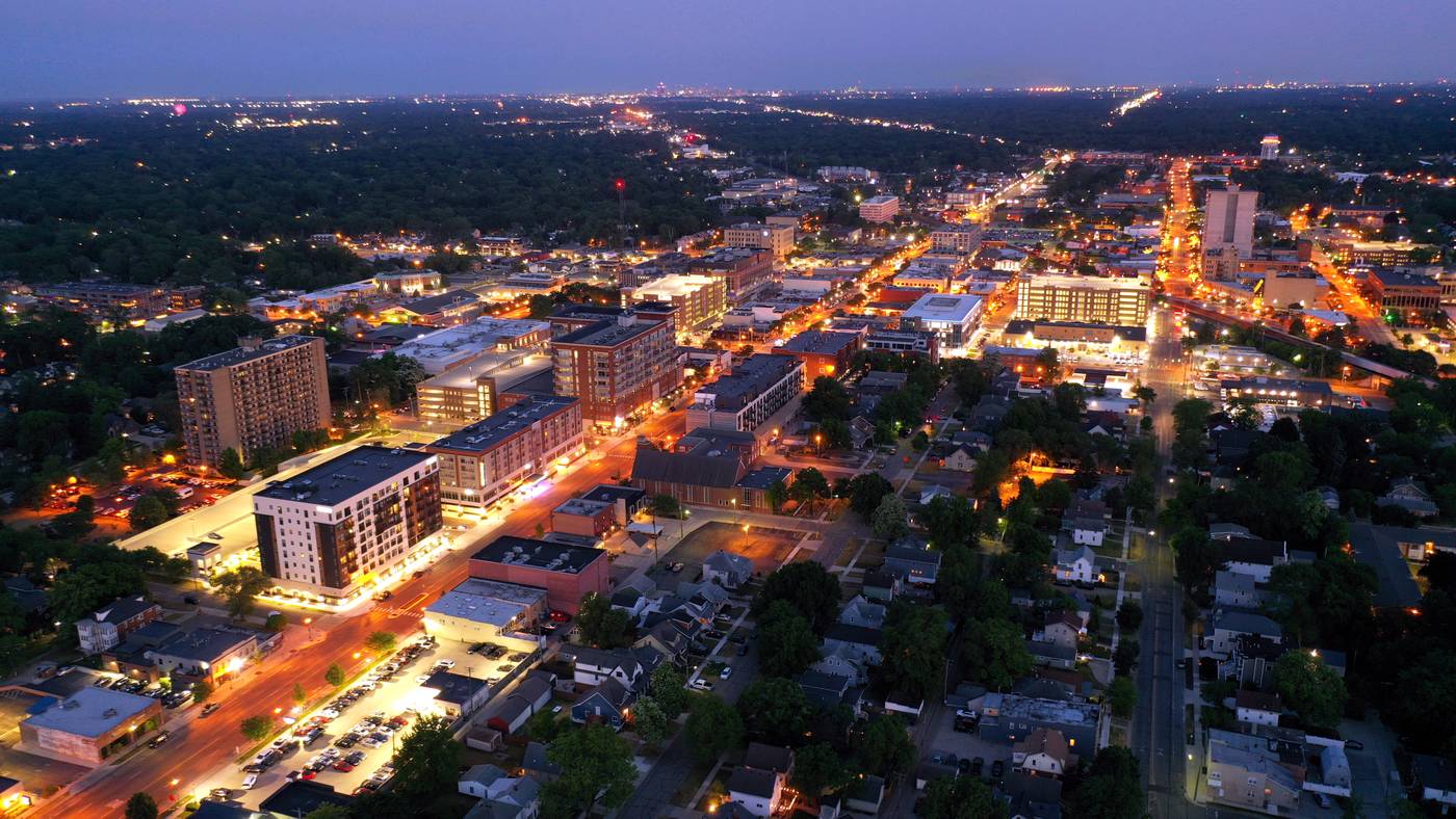 Downtown Royal Oak lit up at dusk from the air, Main Street glowing toward the Detroit skyline