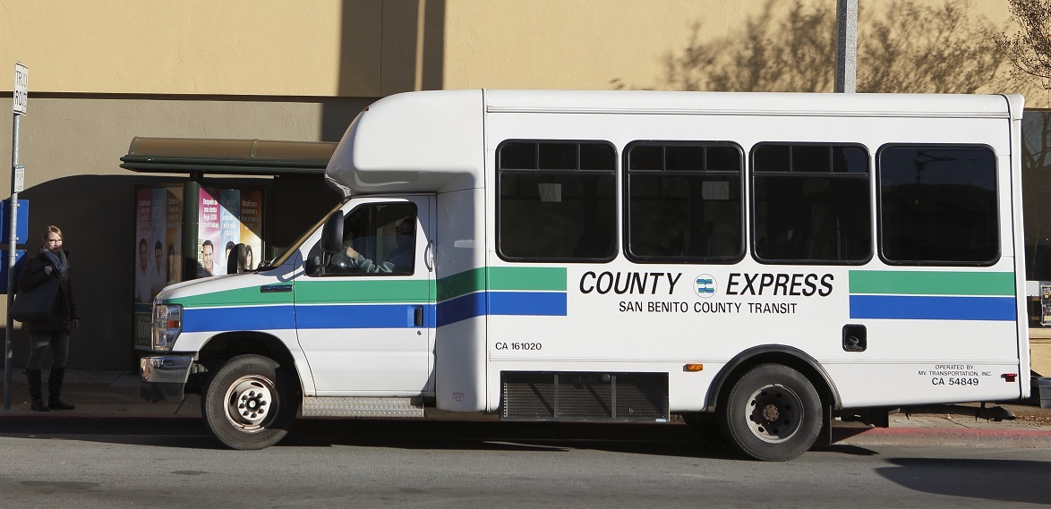 A white County Express bus stopped at the curb, with the blue and green fleet livery visible along its side