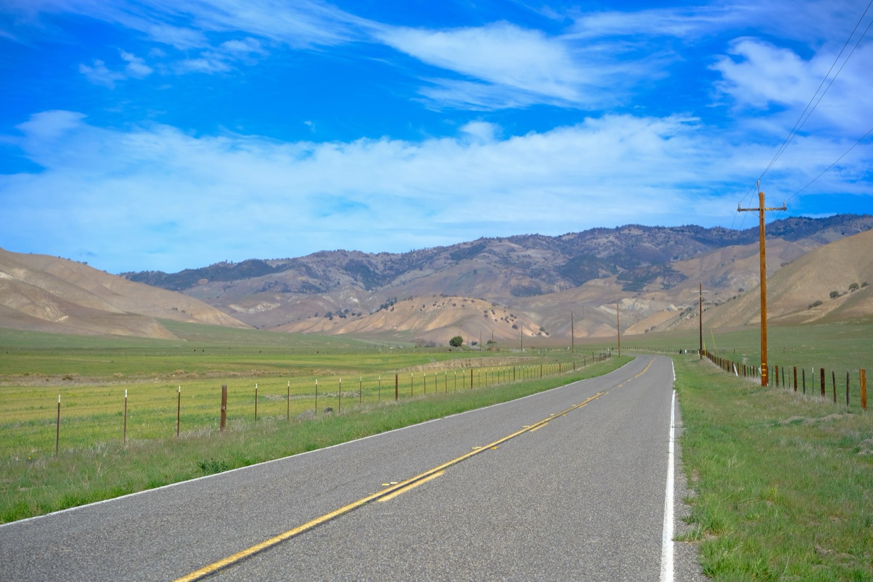 Two-lane State Route 25 running between fence lines and the dry gold hills of San Benito County