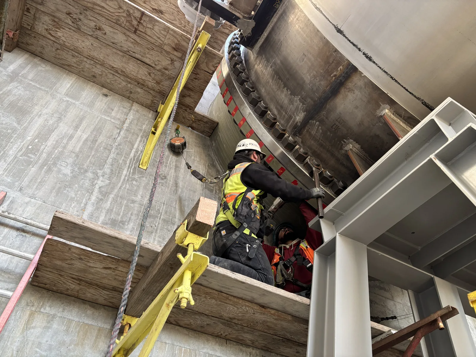 A hard-hatted worker in high-visibility clothing torquing bolts on a large fixed-cone valve, with a second worker below