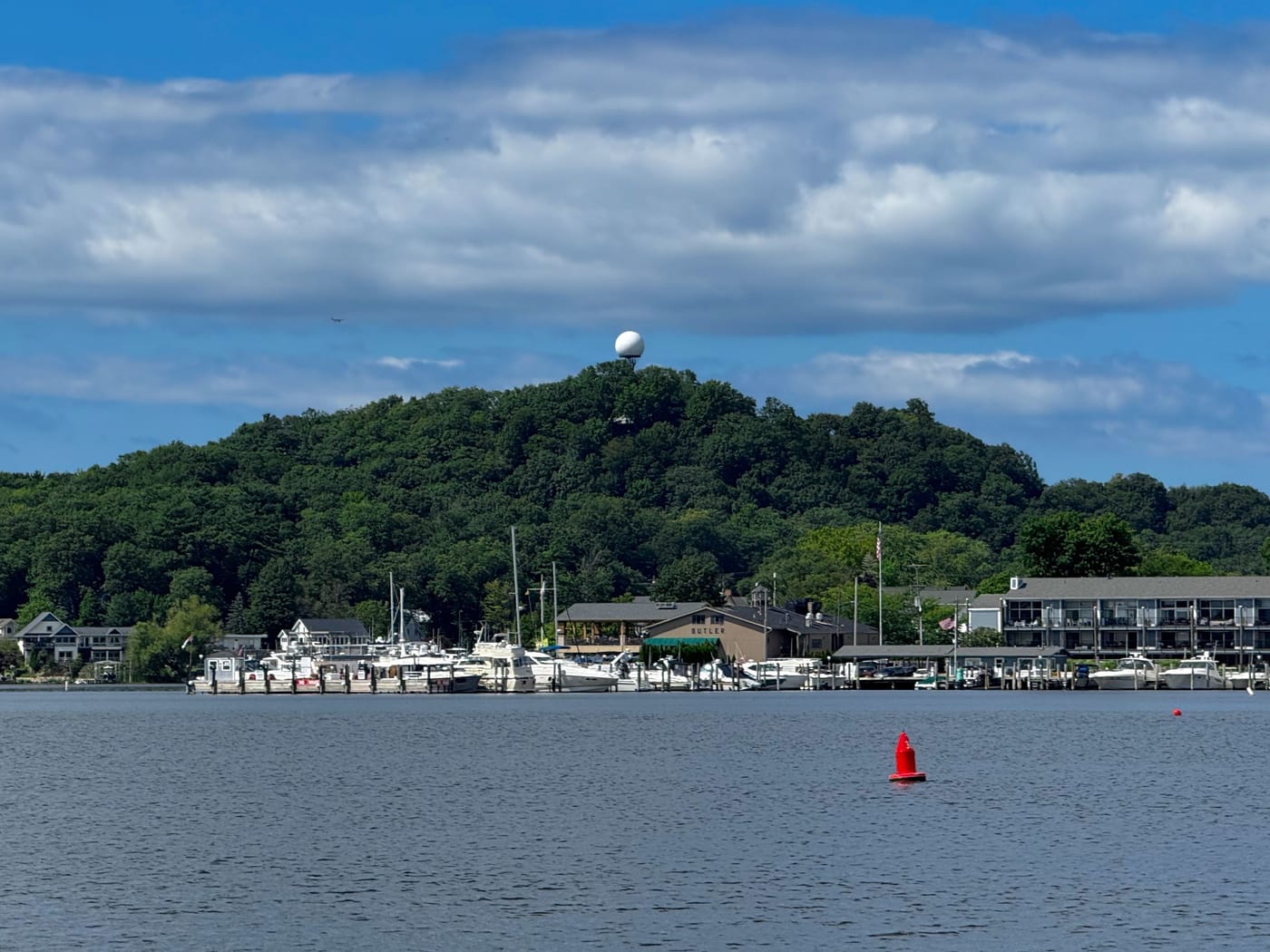 The wooded dune of Mt. Baldhead, a white dome at its top, rising behind the marina and the boats on the Kalamazoo River.