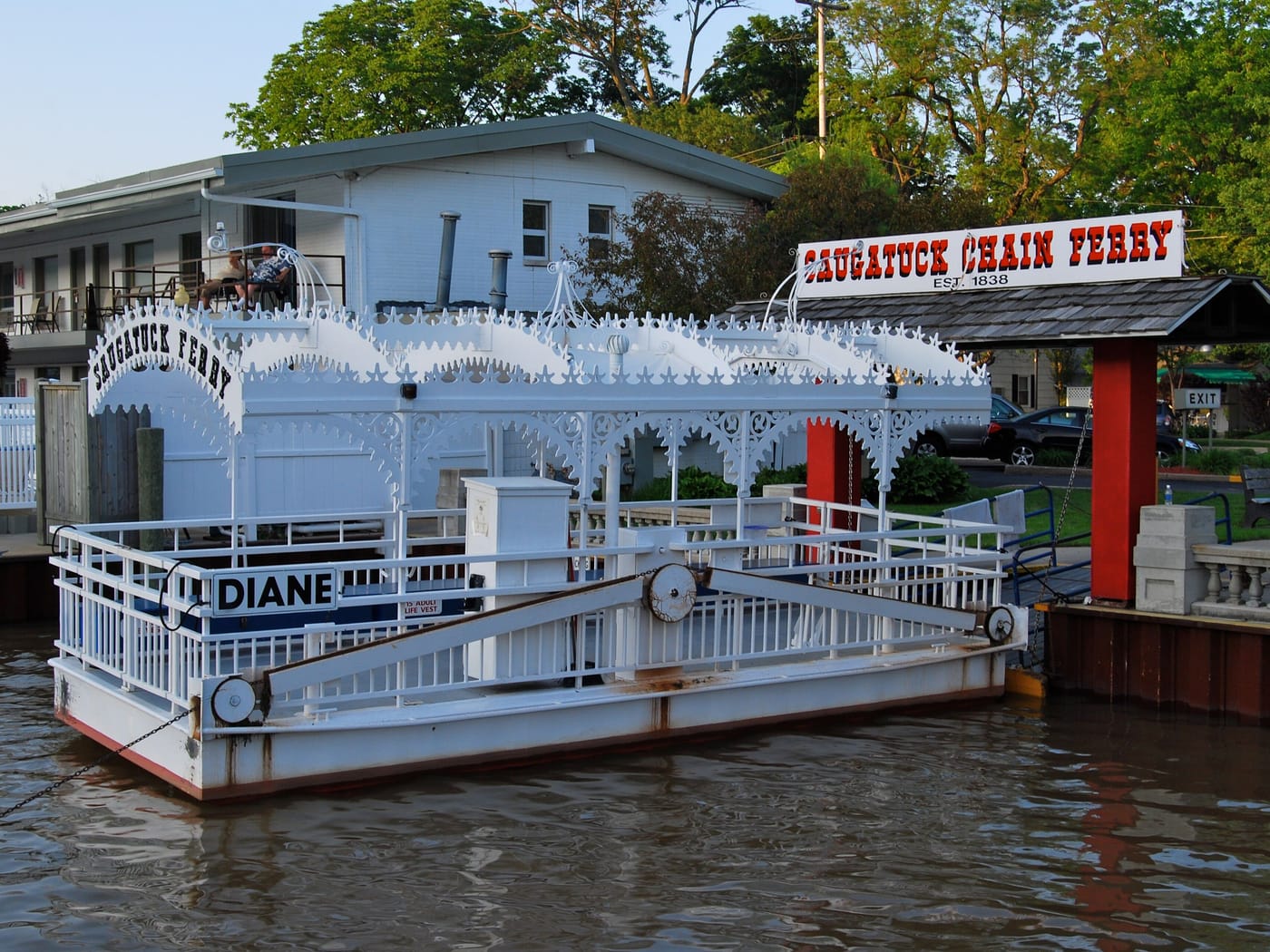 The white chain ferry Diane, trimmed in gingerbread railings, tied up at its landing under the red Saugatuck Chain Ferry sign.
