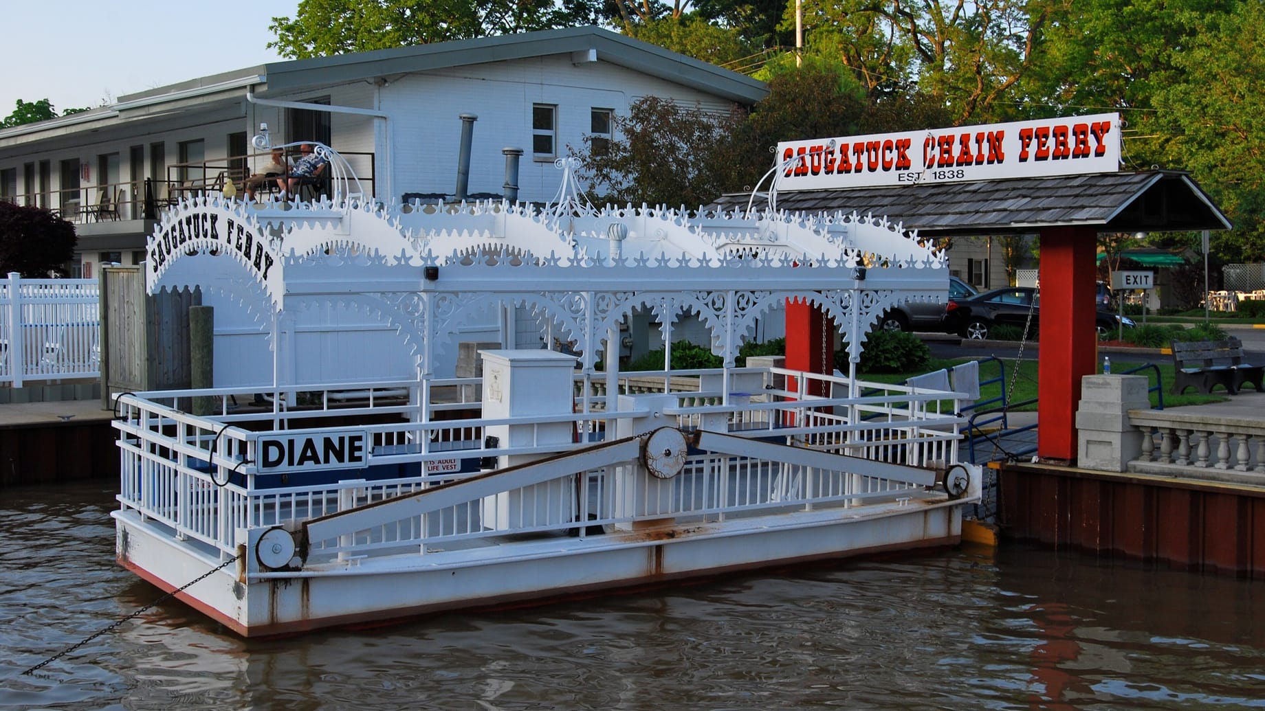 The white chain ferry Diane, trimmed in gingerbread railings, tied up at its landing under the red Saugatuck Chain Ferry sign.