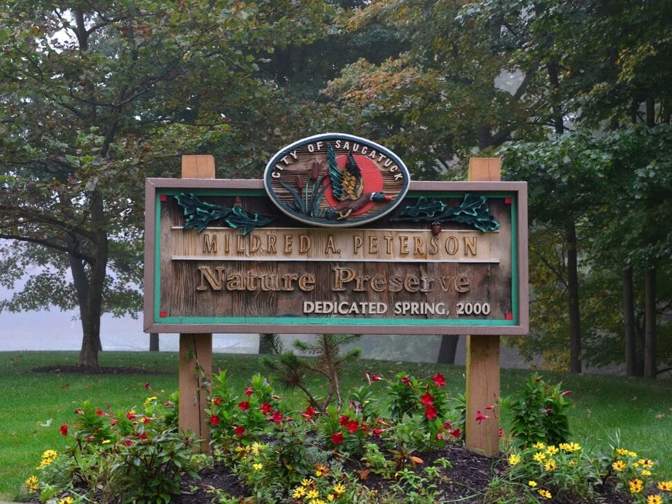 The carved wooden sign of the Mildred A. Peterson Nature Preserve, dedicated spring 2000, above beds of red and yellow flowers.
