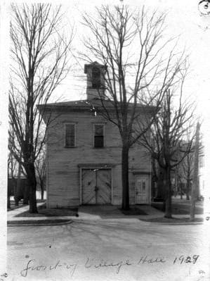 A black-and-white photograph of the two-story clapboard Village Hall in 1929, with its bell cupola, double doors, and bare trees, captioned by hand “Saugatuck Village Hall 1929.”