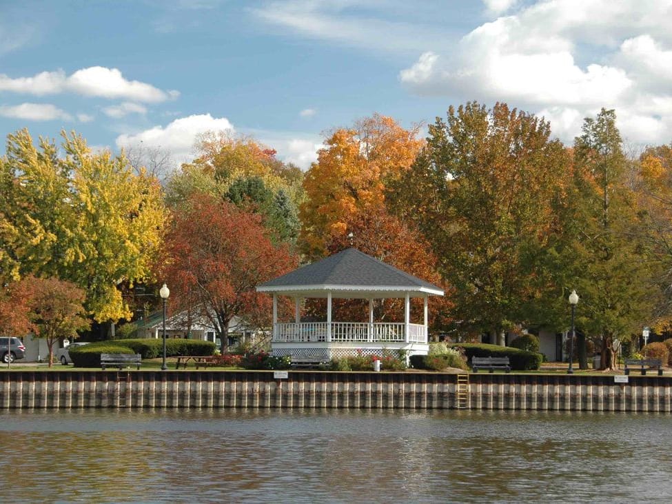 The white Wicks Park gazebo on the river seawall, among trees turning yellow, orange, and red.