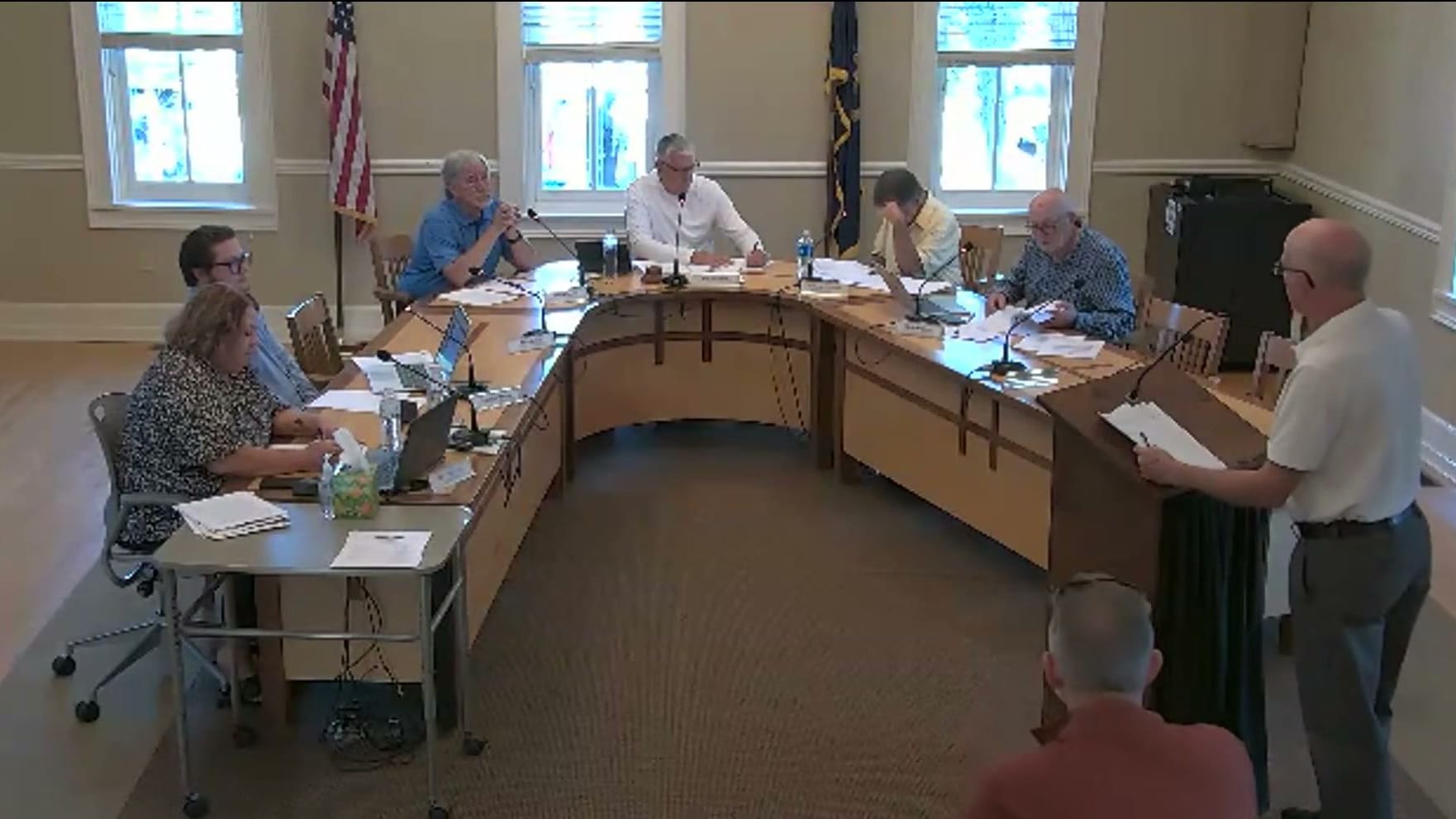 A resident at the podium reads from his papers to the Zoning Board of Appeals, its members seated around the curved dais in the council chambers at City Hall, as another resident waits his turn.