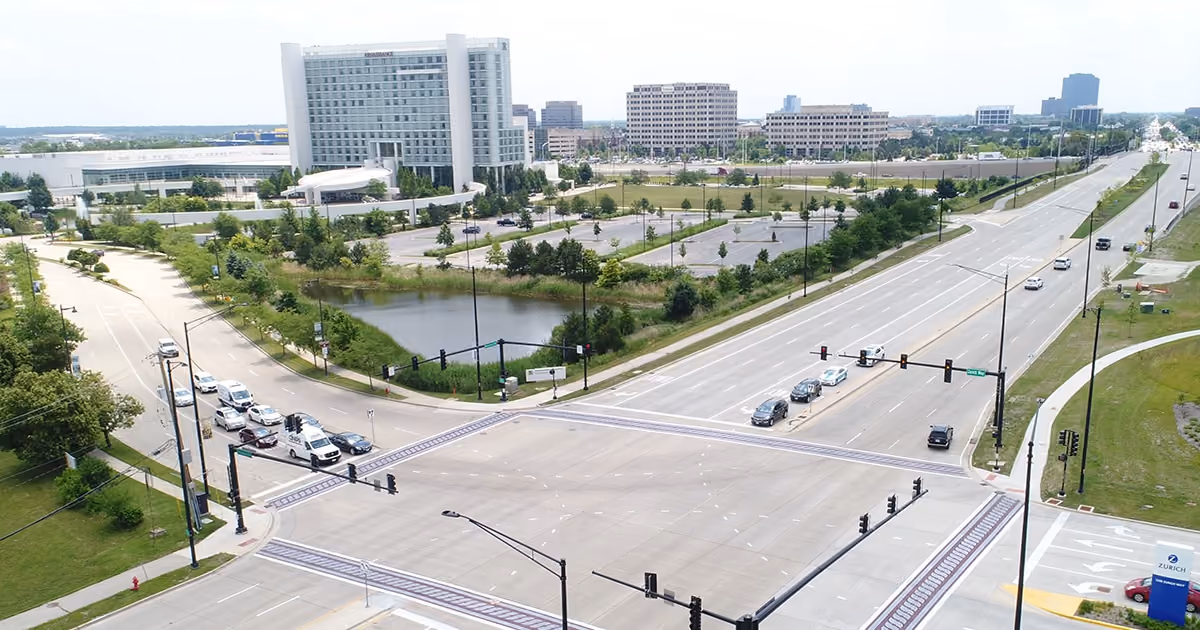Meacham Road and a wide intersection from the air, office towers and a pond along the road