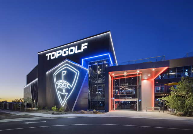 Topgolf Schaumburg at dusk, its sign and entrance lit in blue and red
