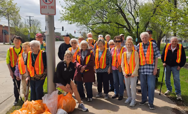 A group of Adopt-a-Bike Path volunteers in orange safety vests beside a bike path, bags of collected litter at their feet