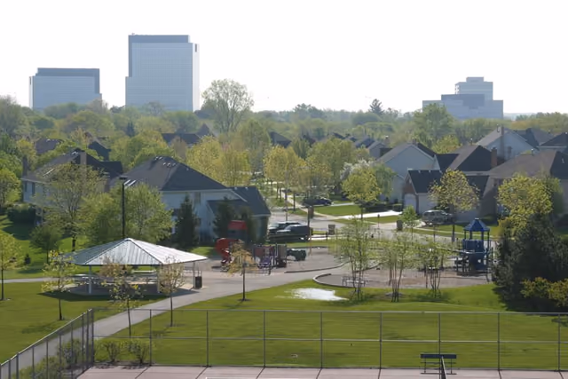 A neighborhood park with a pavilion and paths among houses, office towers on the skyline beyond