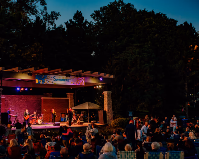 A band playing on Septemberfest's lit local stage at night, a crowd at tables in front