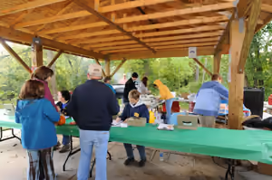 People at a picnic under a wooden pavilion, tables set with green cloths