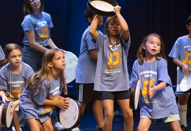 Campers in matching T-shirts playing hand drums on stage