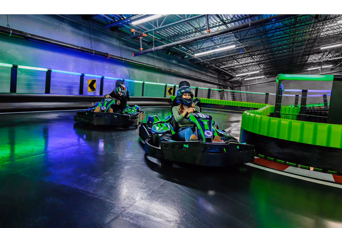 Drivers racing electric karts on Andretti's neon-lit indoor track