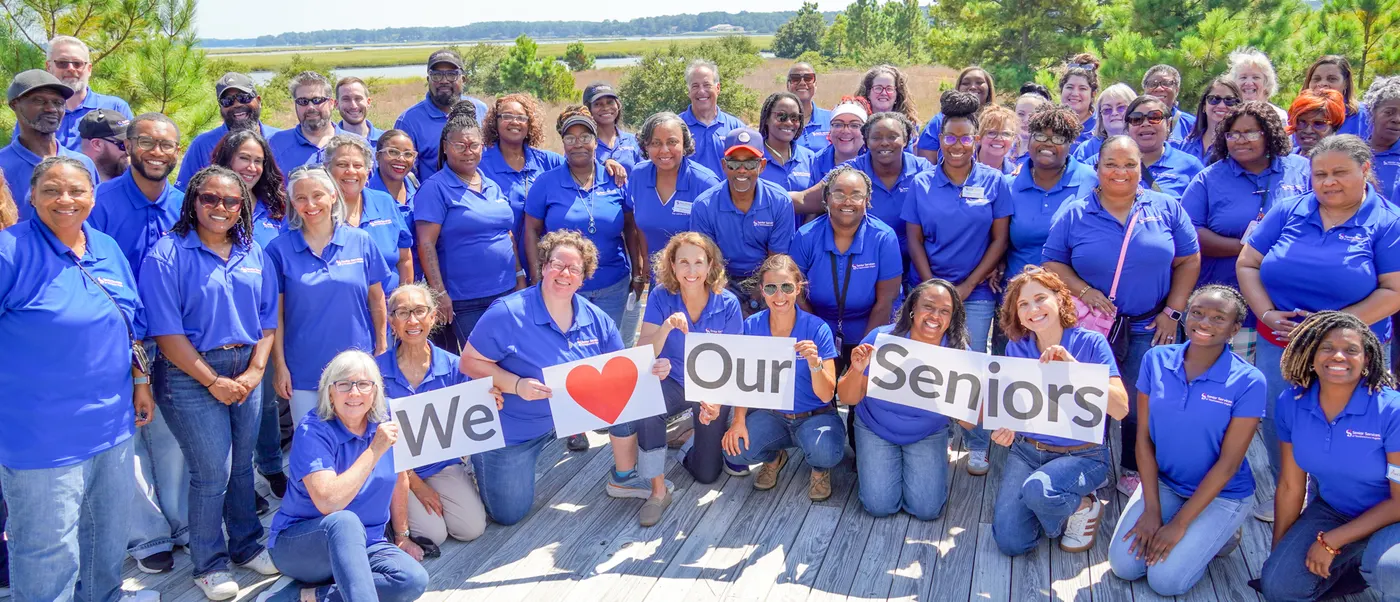 Senior Services of Southeastern Virginia staff gathered outdoors on a boardwalk over coastal marshland, in matching blue polo shirts.