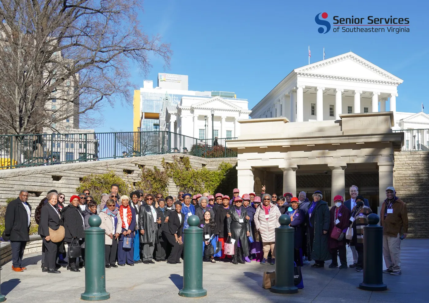 A large group of Senior Services advocates, many of them seniors wearing pink Capitol Hill Club hats, gathered in front of the Virginia State Capitol.