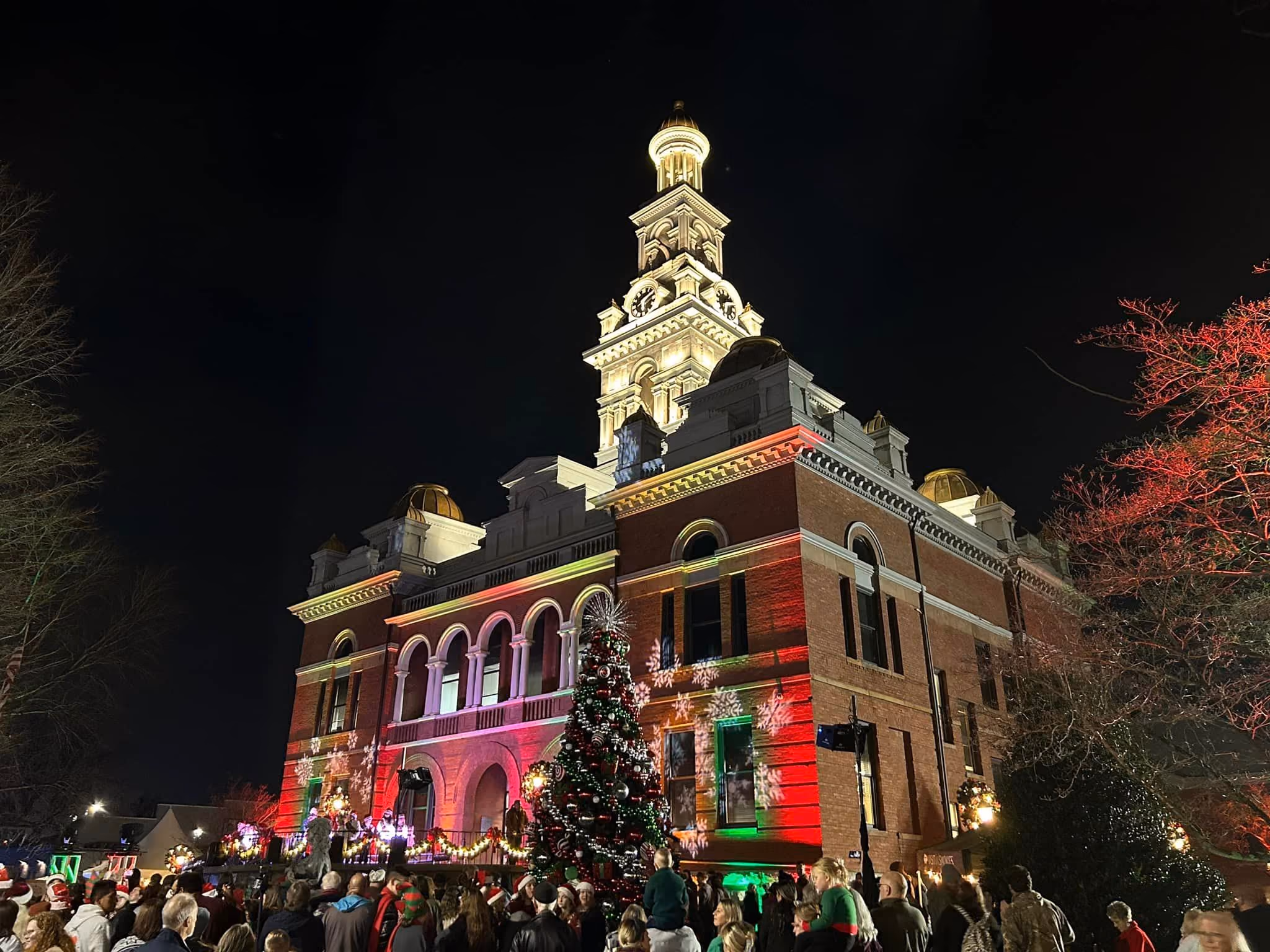Residents on the courthouse lawn at the County's 2023 Christmas tree lighting, the courthouse lit red and green