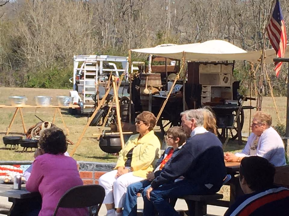 Seniors at outdoor tables beside a chuckwagon cooking camp under canvas