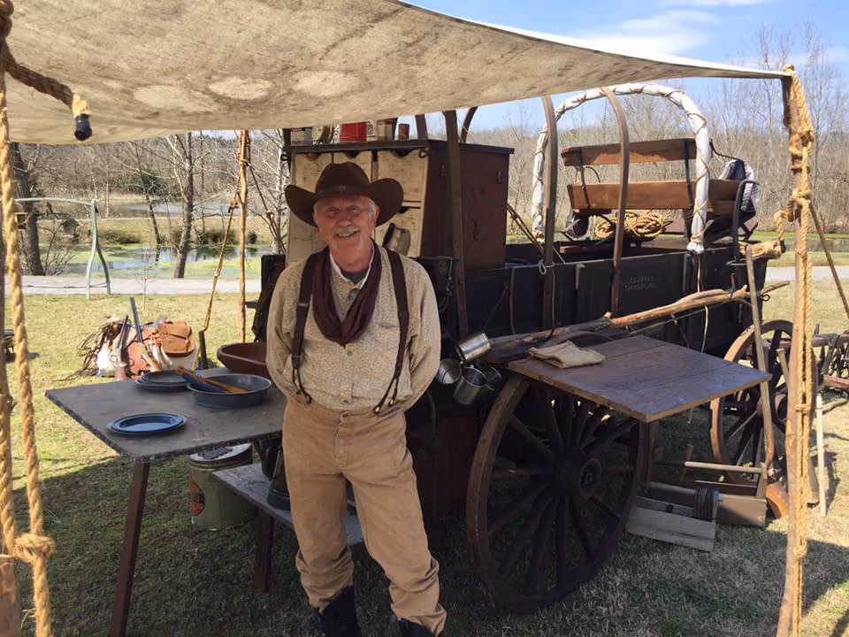 A chuckwagon cook in a cowboy hat and vest beside his wagon