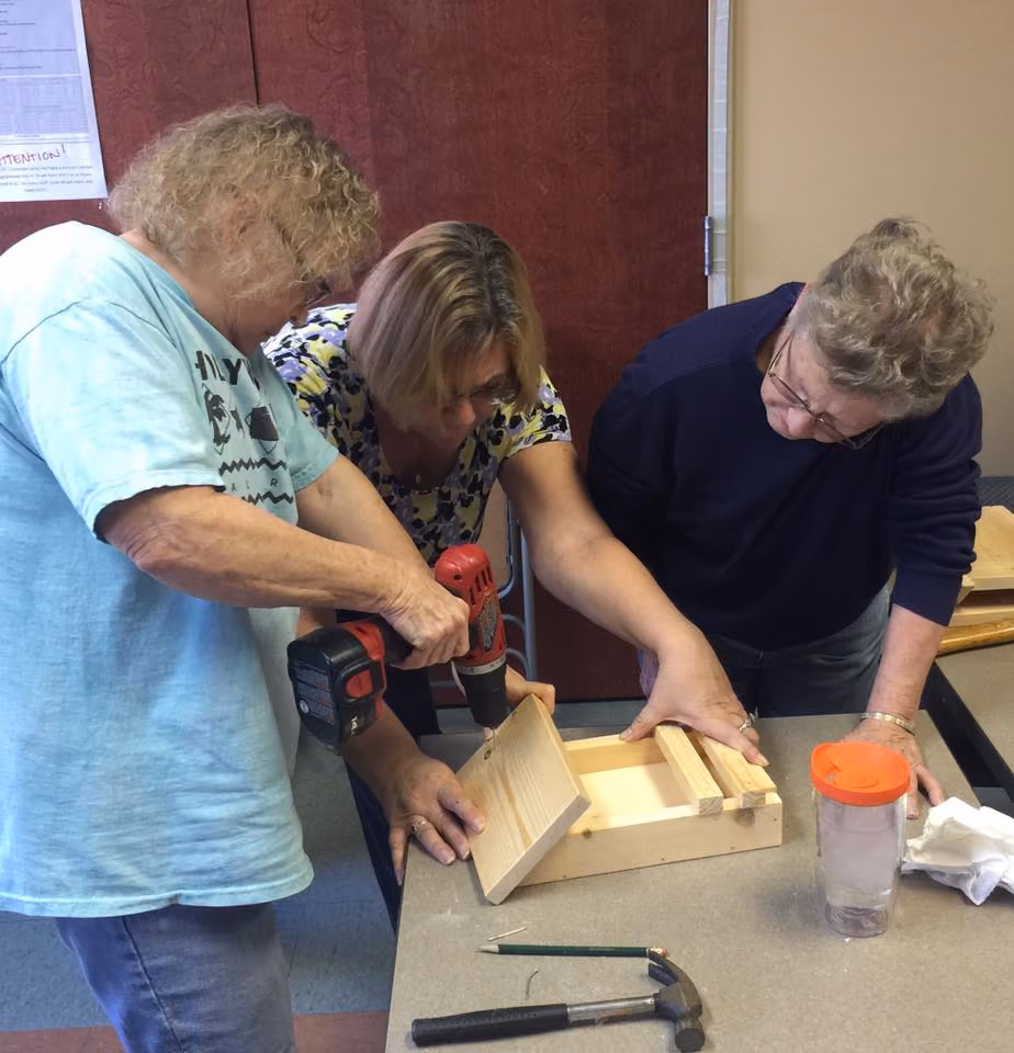 Three women building a small wooden box at a woodworking table