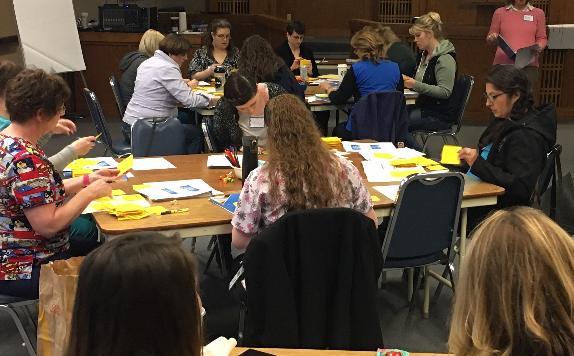 Regional partners work in small groups around tables at a facilitated planning session, sorting cards and notes.