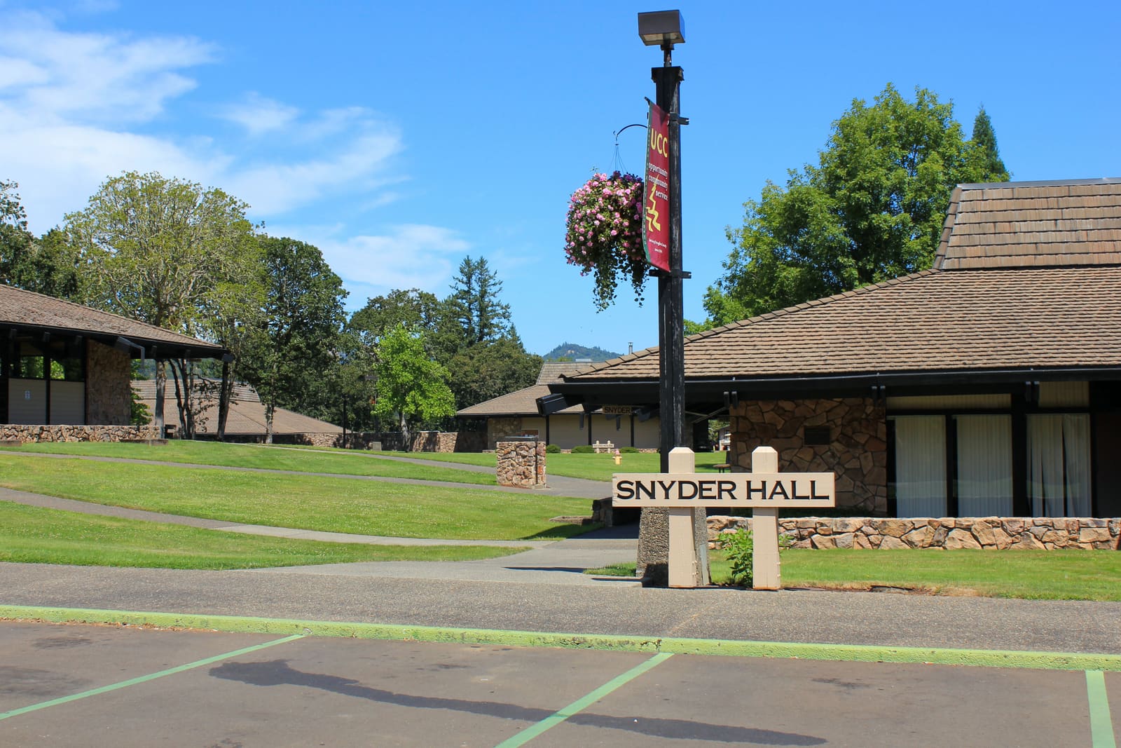 The Snyder Hall name board on the lawn at Umpqua Community College in Roseburg, with the low stone-and-timber building behind it.