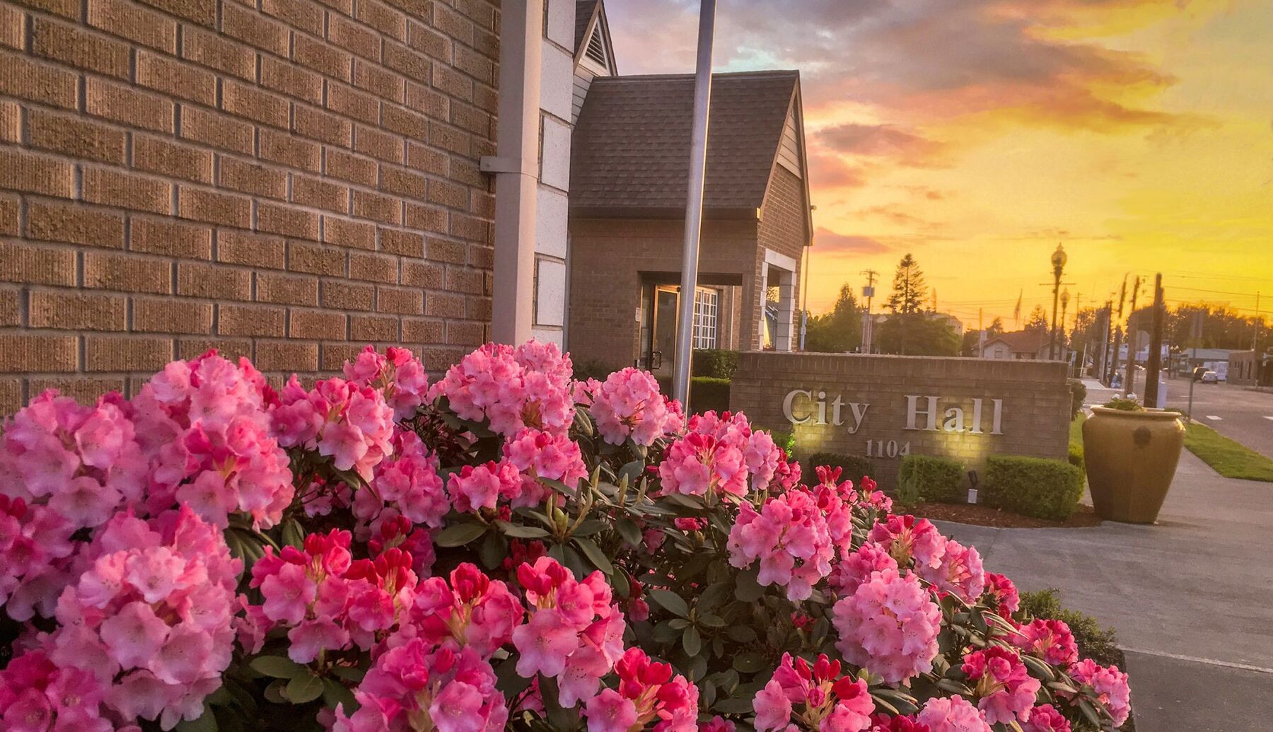 The Sumner City Hall entrance and its brick sign at sunset, framed by blooming pink rhododendrons.