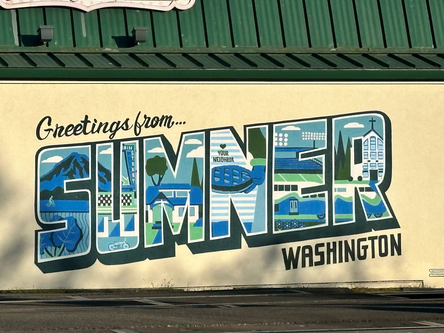 The "Greetings from... Sumner, Washington" large-letter postcard mural painted on a green corrugated building by the tracks.