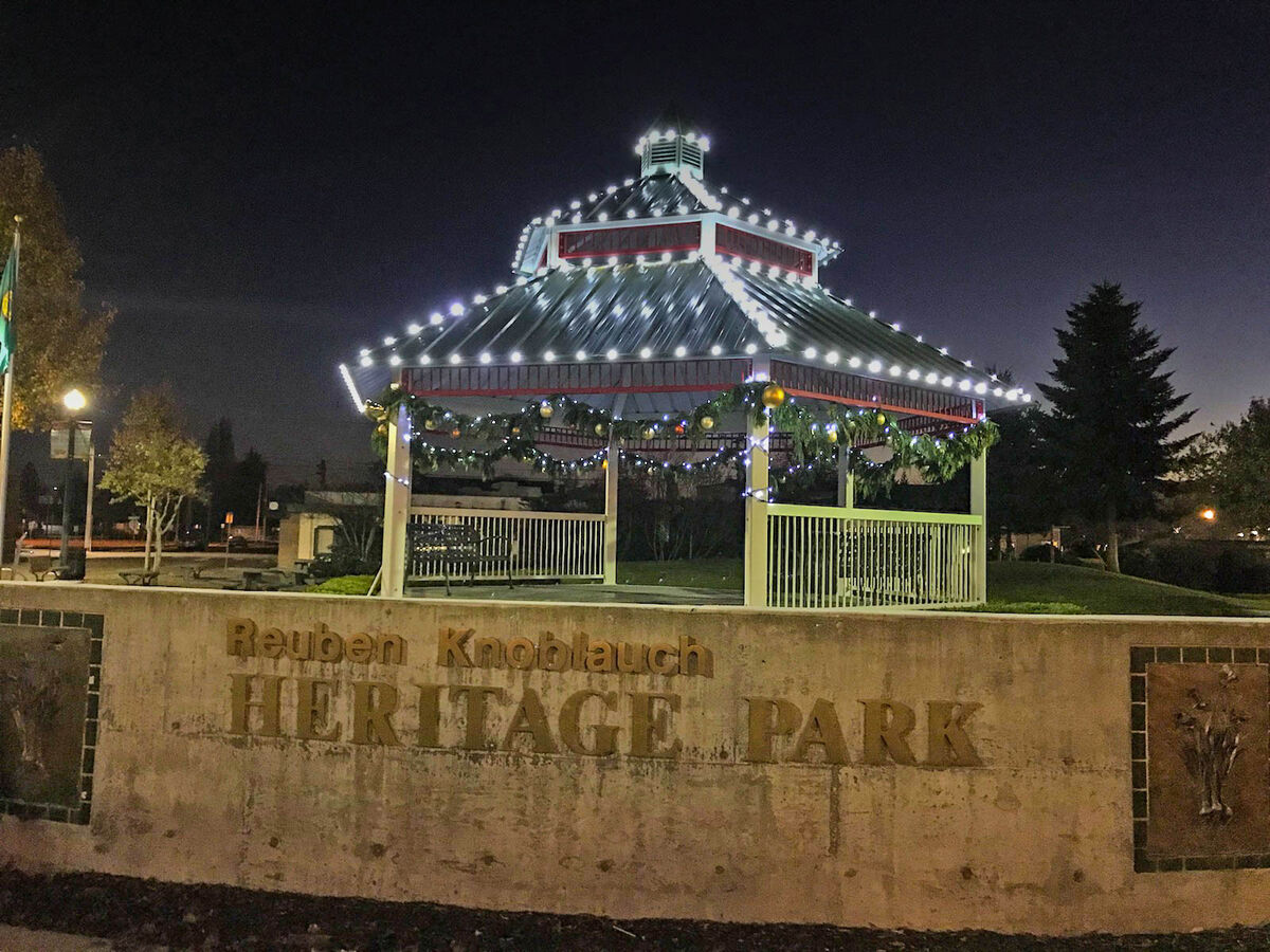 The Reuben Knoblauch Heritage Park stone entrance sign with the gazebo strung in white lights behind it at night.