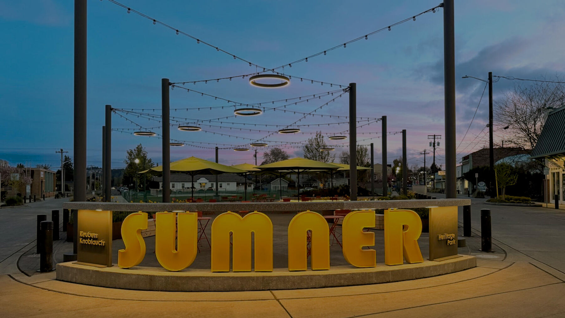 Large illuminated block letters spelling SUMNER at the Heritage Park plaza under string lights at twilight.