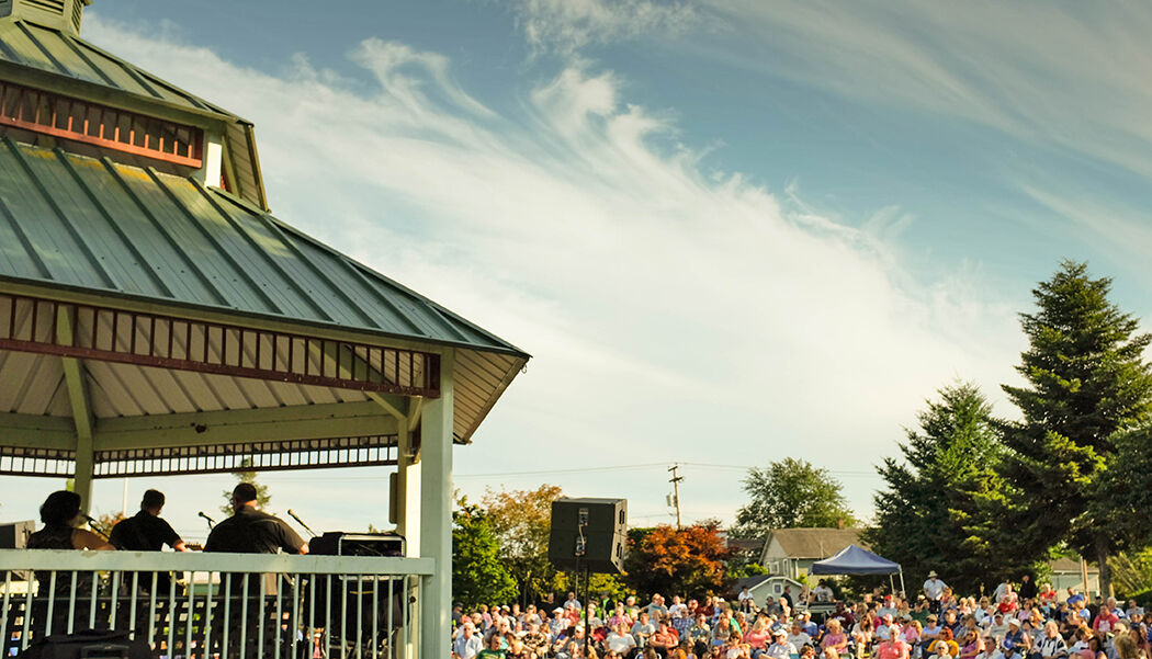 A band performs from the park gazebo bandstand to a crowd seated on the lawn at a Music Off Main concert.