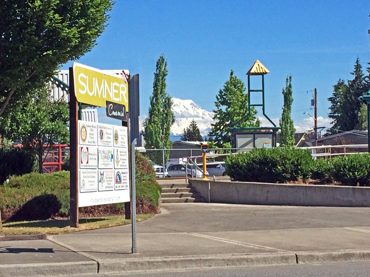 The Sumner Station sign and depot plaza with Mount Rainier rising over the trees behind it.