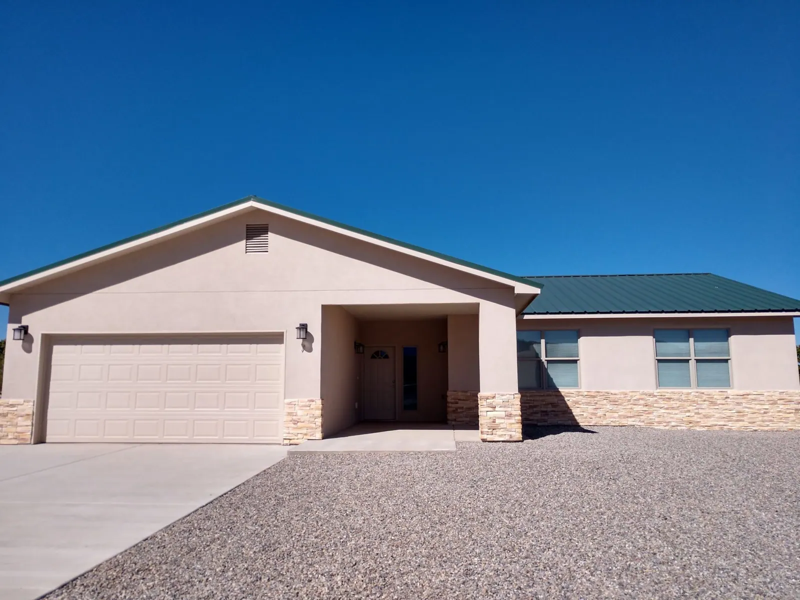 A tan stucco THI home with a stone wainscot and a two-car garage on Eagle Loop, under a deep blue sky.
