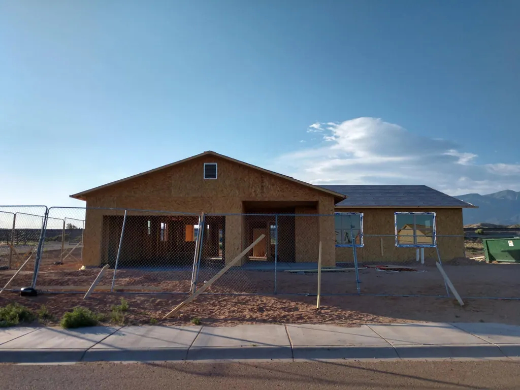 A THI home under construction, its walls sheathed and roof framed, behind a temporary fence.