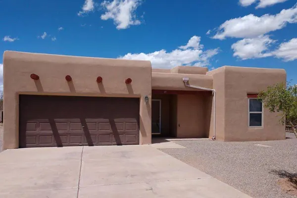 A Pueblo Revival THI home with a flat roof, round vigas along the parapet and a brown garage door.