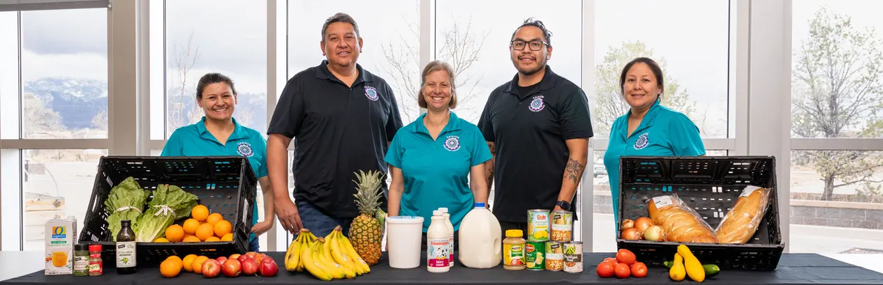 Five members of the Tamaya Wellness Program team stand behind a table of fresh fruit, vegetables and bread.