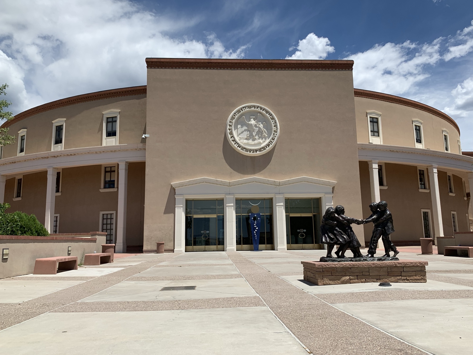The round, adobe-toned New Mexico State Capitol building in Santa Fe, the Great Seal mounted above its entrance under a bright sky