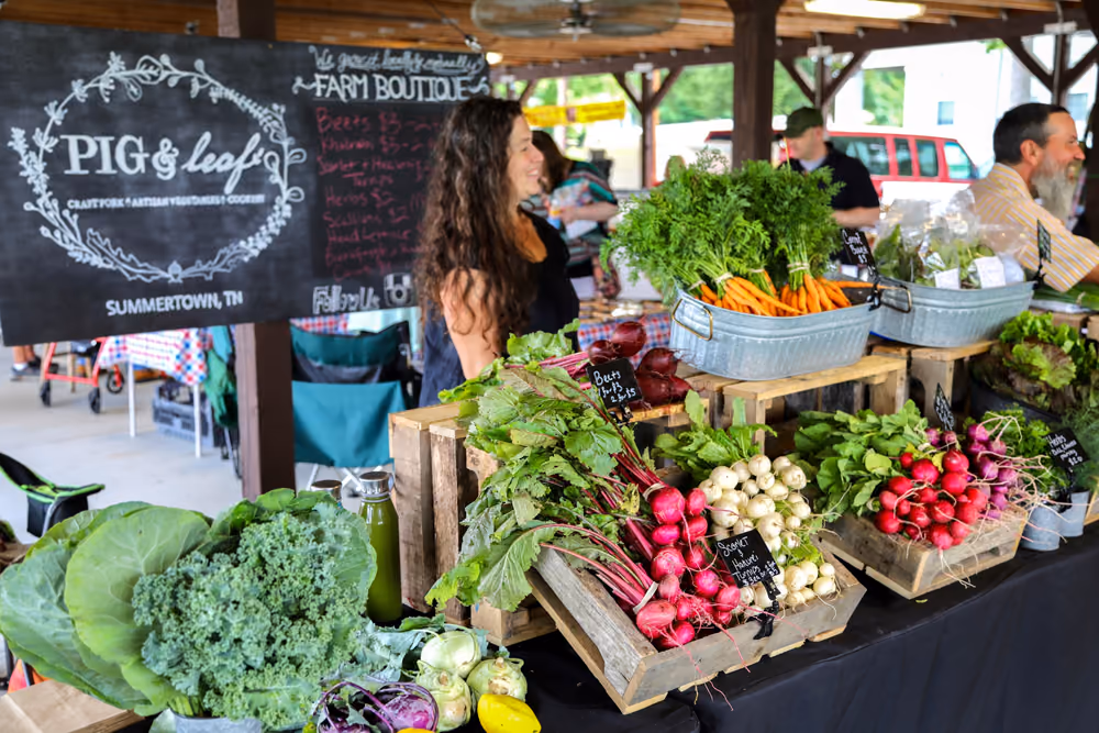 A vendor at the farmers market behind crates of radishes, beets and greens.