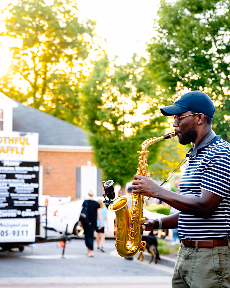 A saxophonist playing on the sidewalk at First Fridays beside a food truck.