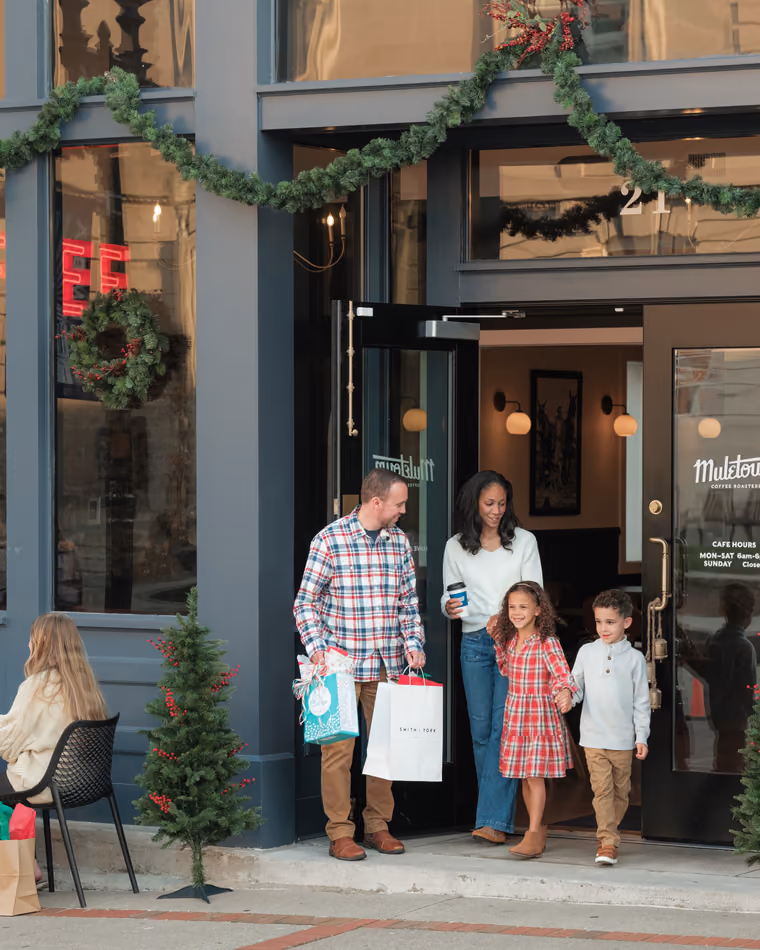 A family with shopping bags leaving Muletown Coffee, its windows hung with Christmas wreaths.
