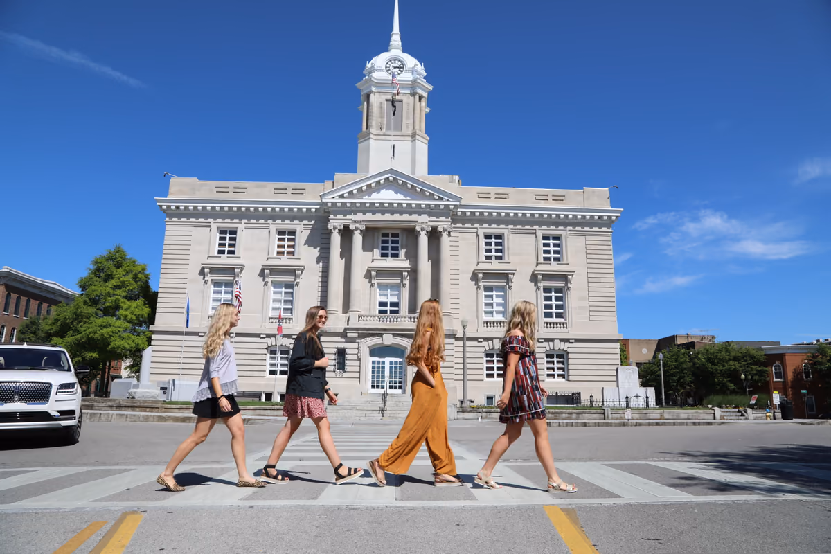 Four friends crossing the street in front of the Maury County Courthouse on a sunny day.