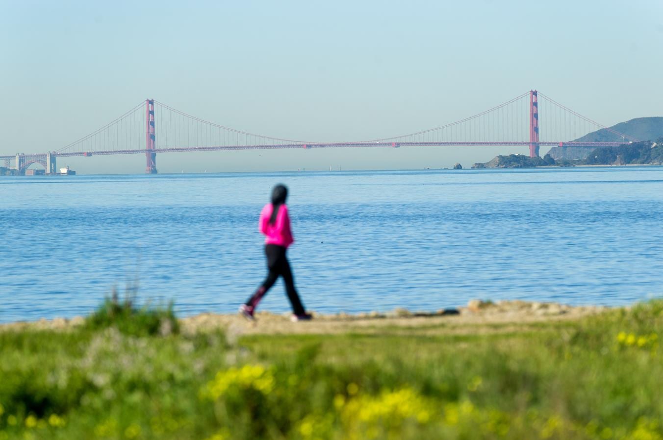 A walker on the Richmond shoreline of the San Francisco Bay Trail with the Golden Gate Bridge beyond