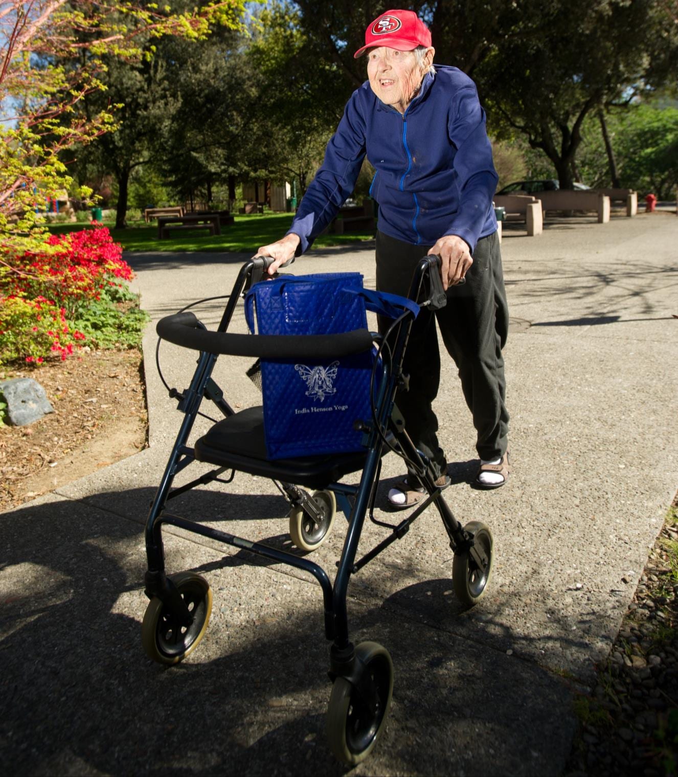 An older adult walking a paved park path with a rolling walker