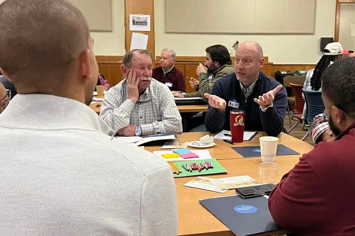 Members of a faith community talk around tables in a church fellowship hall.