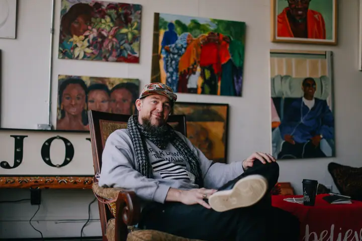 Elias Moreno Lothe sits back in an armchair below a wall of painted portraits.